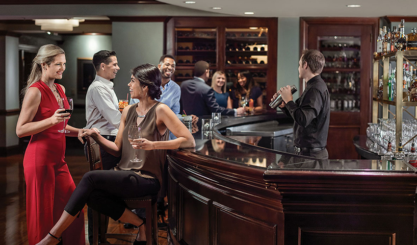 A bartender shakes a cocktail while patrons socialize at a bar.