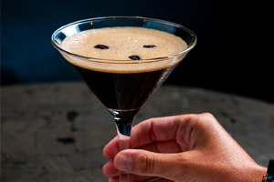 A hand holds a martini glass filled with an espresso martini topped with three coffee beans.