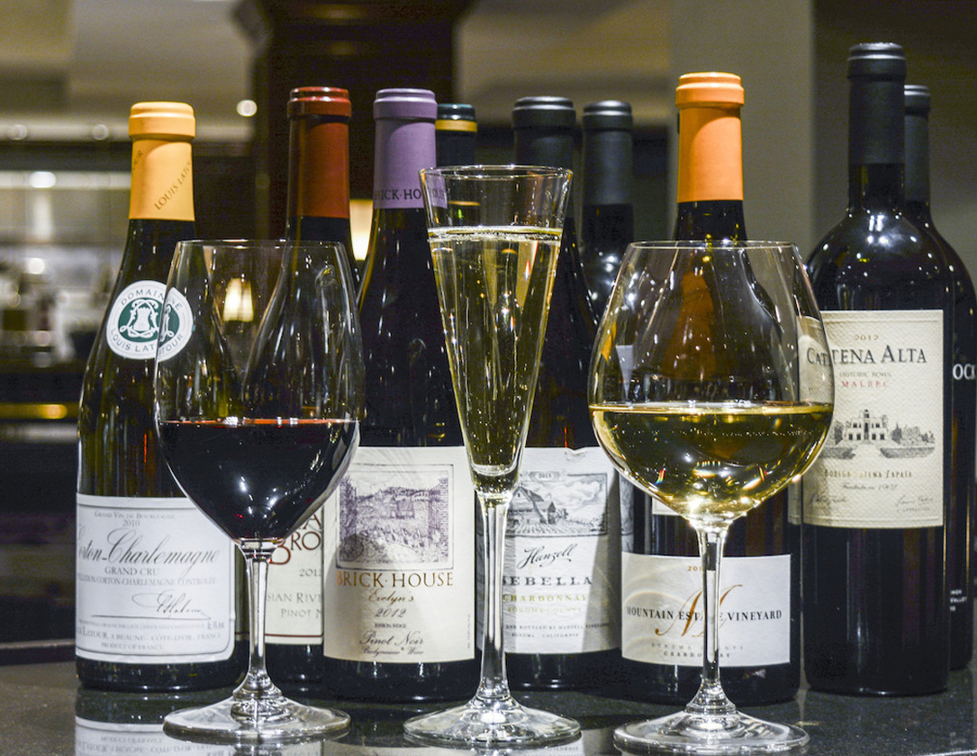 Several bottles of wine and glasses of red, white, and sparkling wine are displayed on a dark surface.