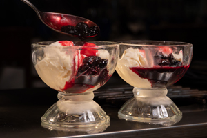 Two glasses of vanilla ice cream topped with a berry compote and syrup.