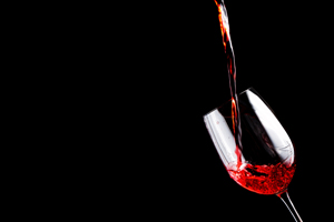 Red wine being poured into a wine glass against a black background.