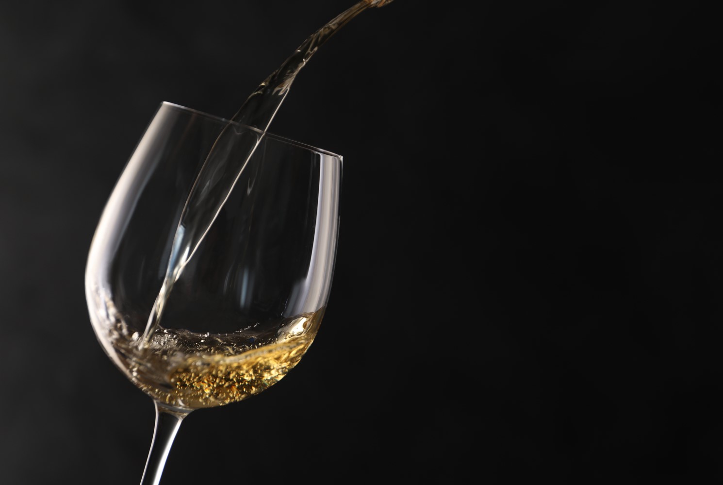 White wine being poured into a tilted wine glass against a plain black background.