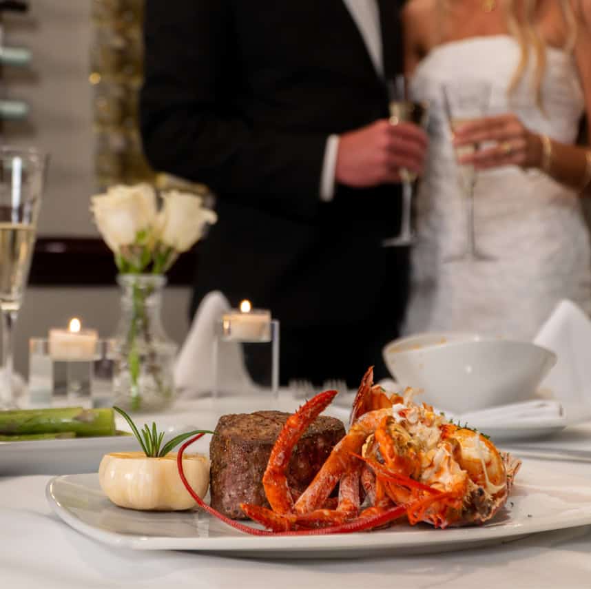A gourmet surf and turf dinner featuring a grilled lobster tail and filet mignon, served with asparagus and champagne.
