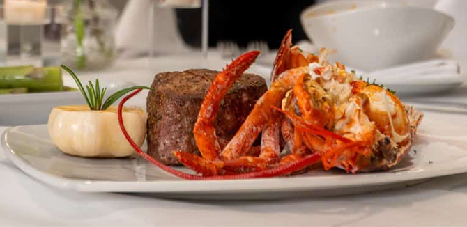 Seared fish fillet with a rich orange sauce, black lentils, asparagus, and garnishes on a white plate.