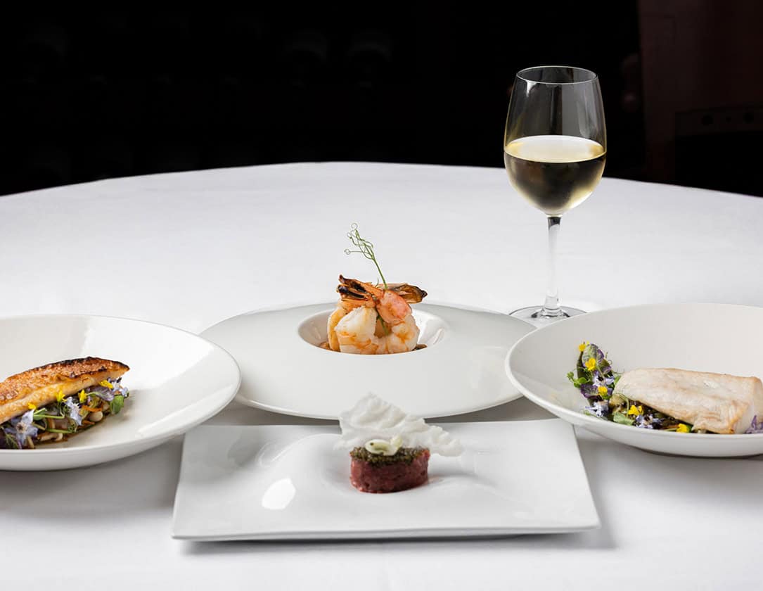 Gourmet seafood tasting menu with wine, featuring shrimp, fish, and tartare.